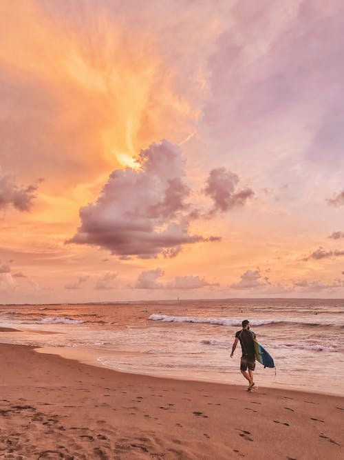 Pria Berjalan Di Pantai Sambil Memegang Papan Selancar