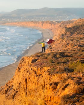 Man holding flag on stunning Baja California cliffs with ocean view.