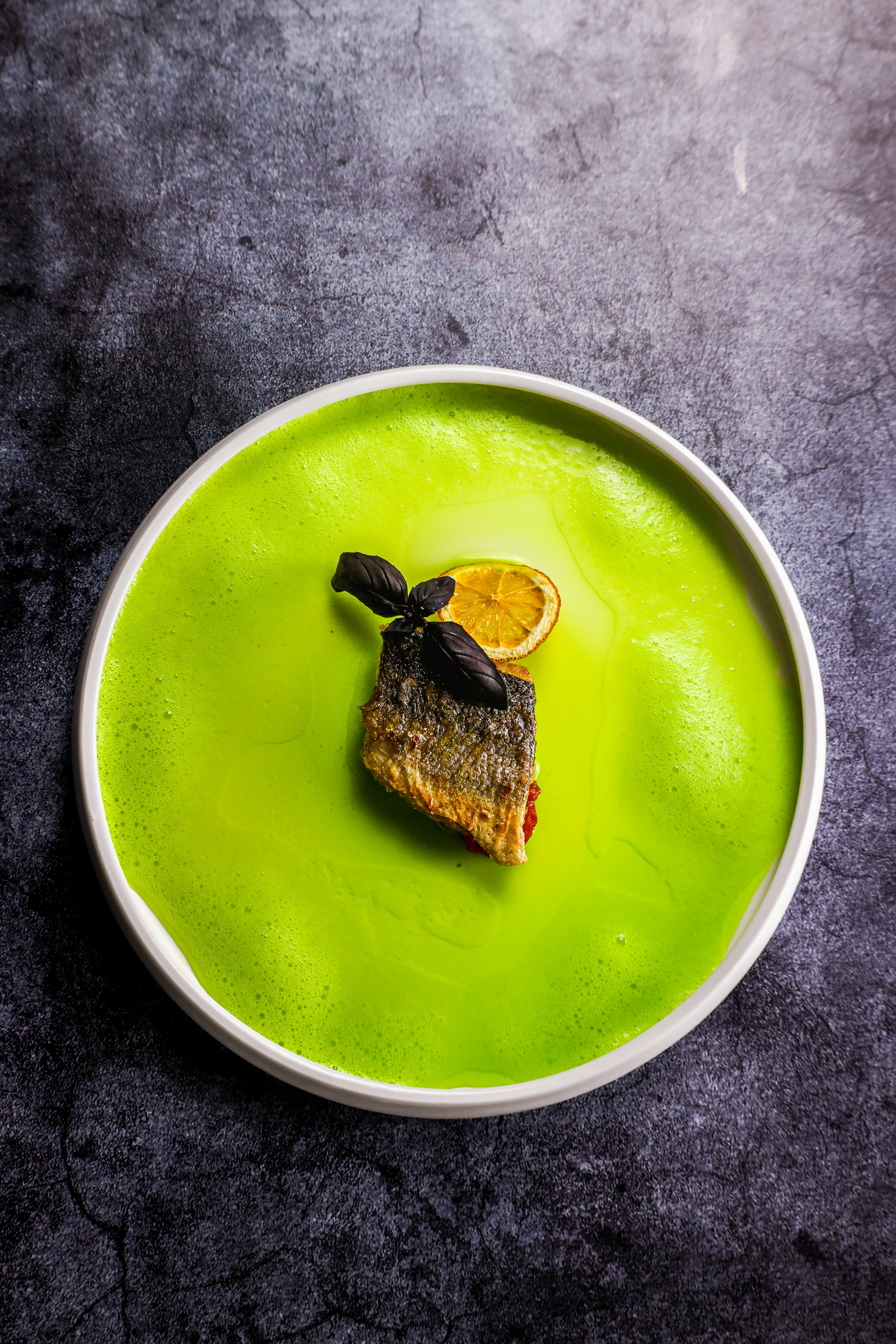 Elegant presentation of a fish fillet with lemon and herbs in a vibrant green sauce.