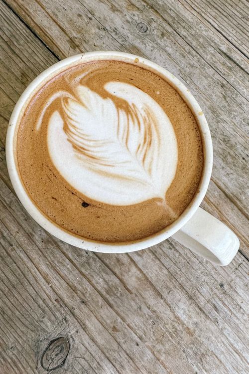 Free Top-down view of a latte with a feather design in the froth, placed on a rustic wooden table. Stock Photo