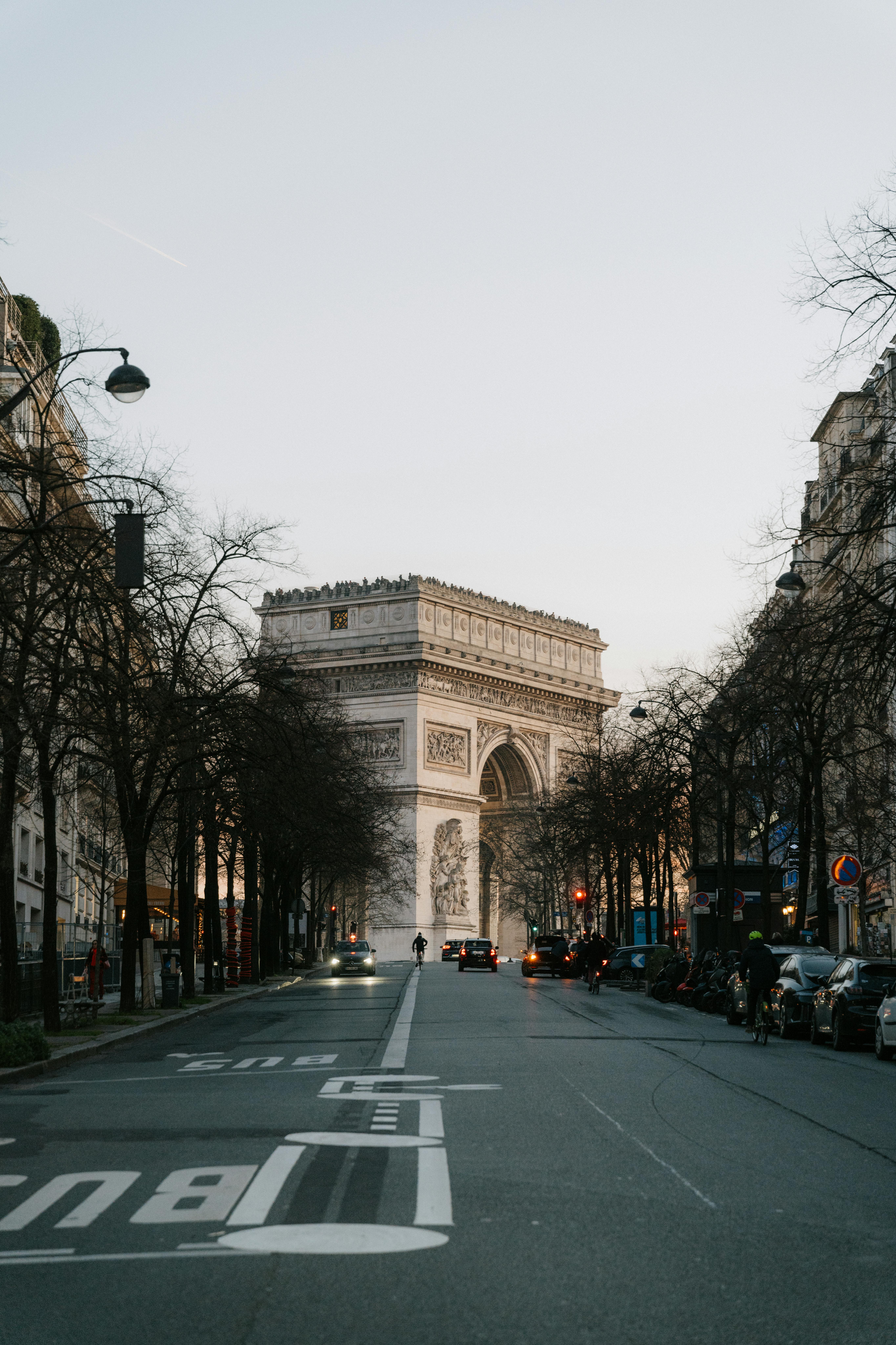 Street view of Arc de Triomphe at sunset with soft light and evening traffic in Paris.