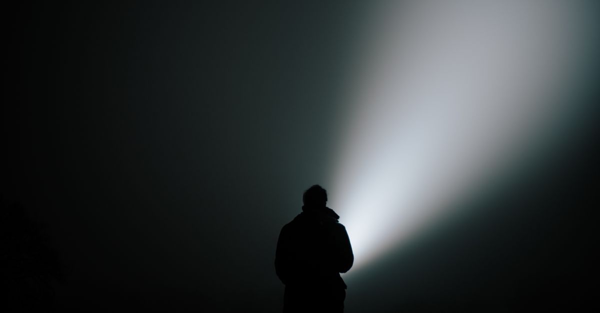 Silhouette of a person in dense fog, illuminated by a bright flashlight.