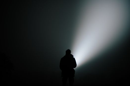 Silhouette of a person in dense fog, illuminated by a bright flashlight.