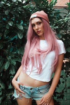 Portrait of a stylish woman with pink hair in casual summer attire posing outdoors.