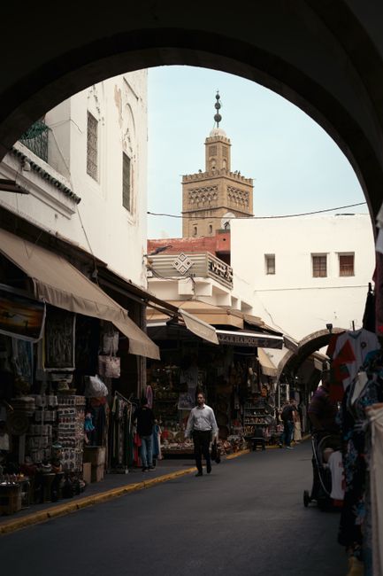 Vibrant street market scene in a historic medina with a mosque tower in the background.
