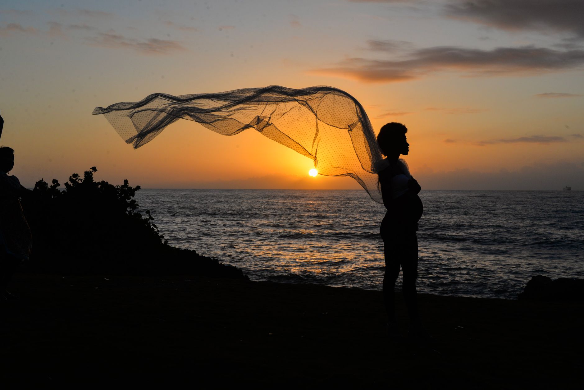 Silhouette of a pregnant woman with scarf at sunset by the sea. Peaceful and contemplative scene.