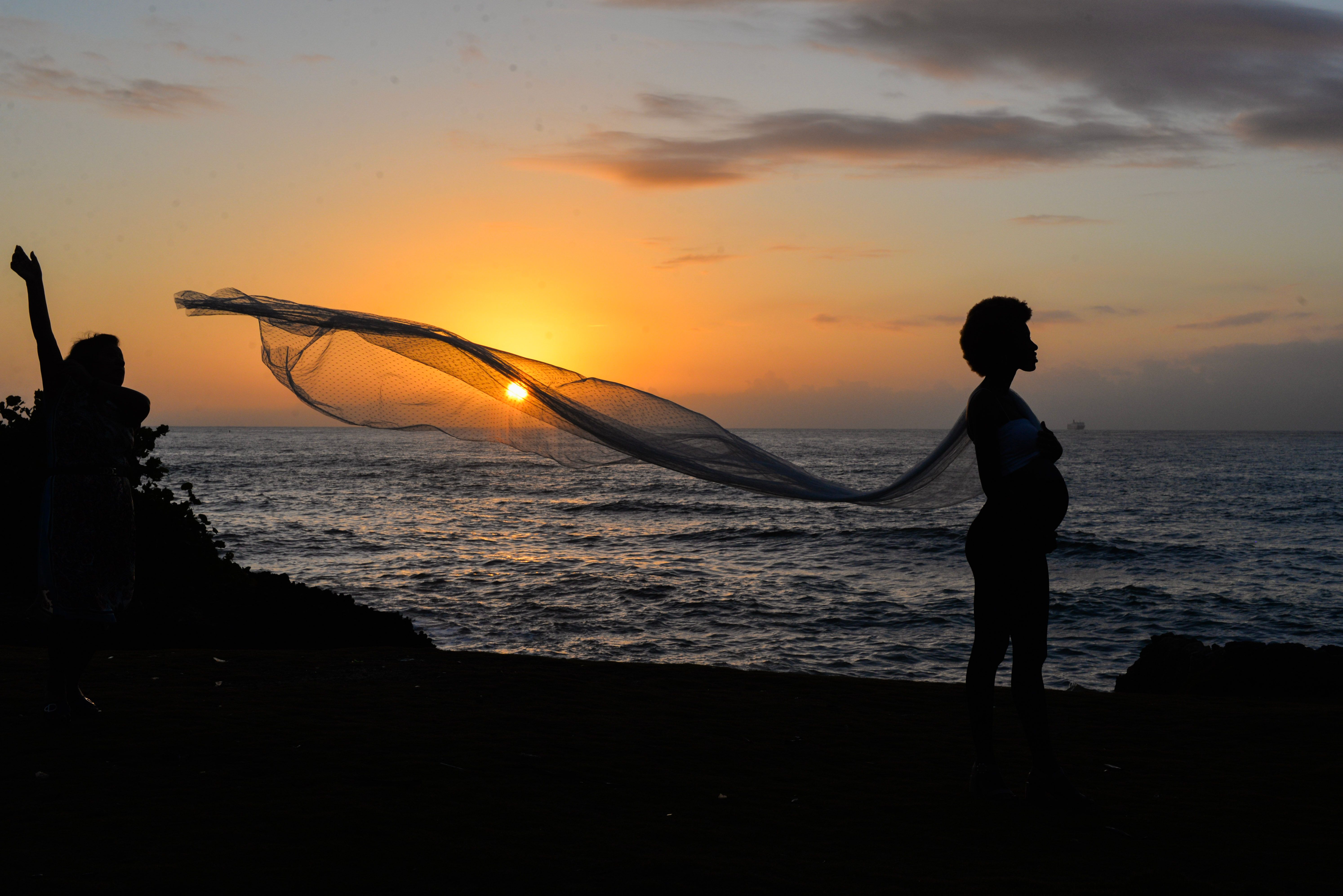 A stunning silhouette of a pregnant woman by the sea at sunset. Peaceful and serene scenery.