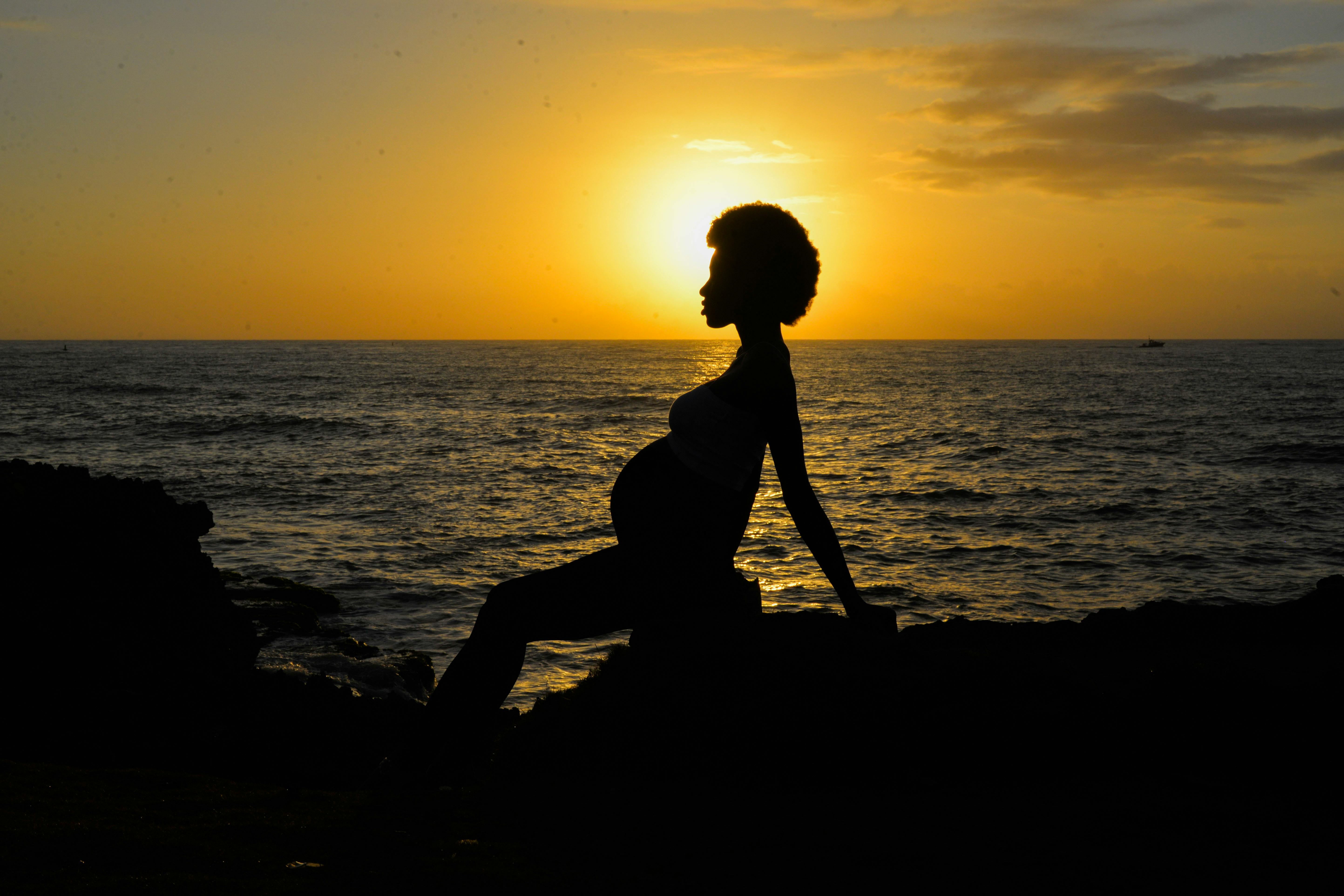 Pregnant woman silhouette on the coast at sunset, reflecting tranquility and beauty.