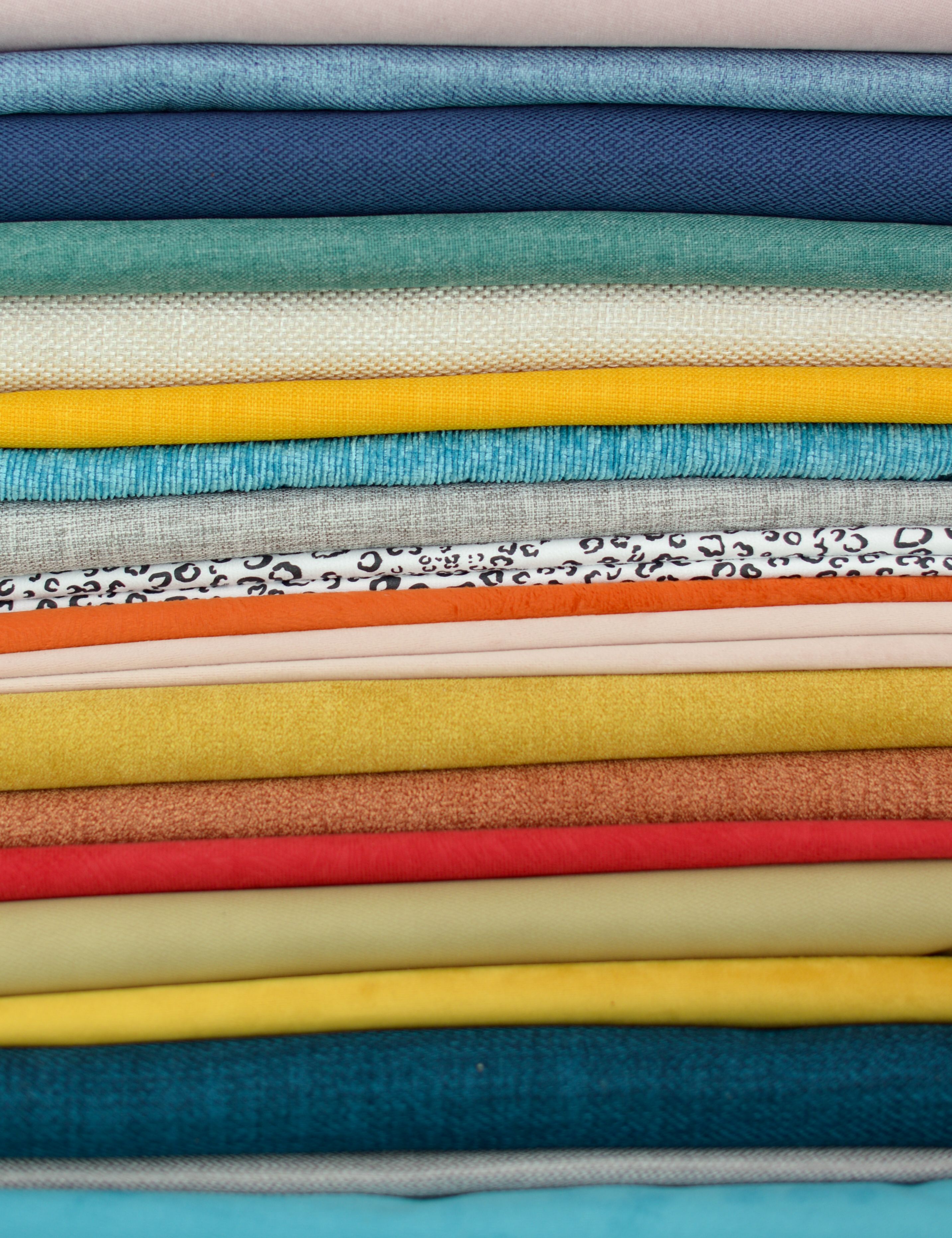 A variety of colorful fabrics stacked horizontally showcasing diverse textures and patterns.