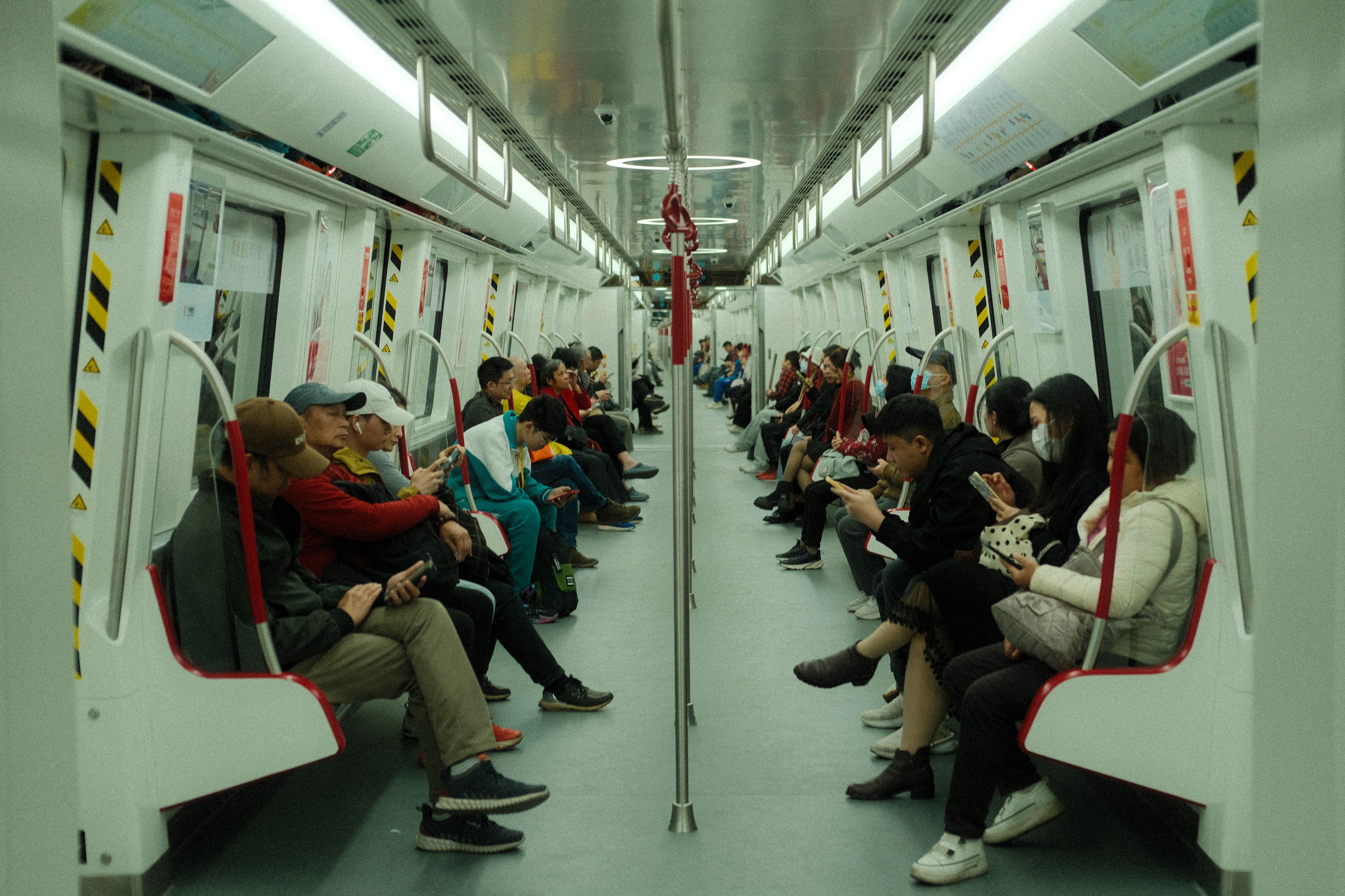 Passengers on a modern subway train using smartphones during daytime commute.