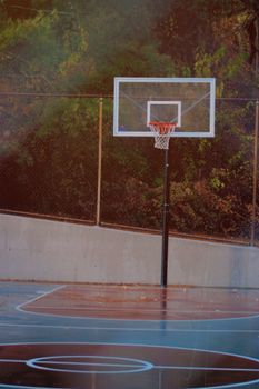 A solitary outdoor basketball hoop in an empty court surrounded by trees.