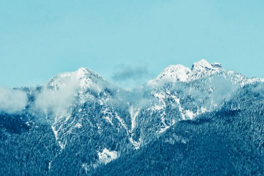 Stunning snow-covered mountain peaks surrounded by soft, misty clouds.