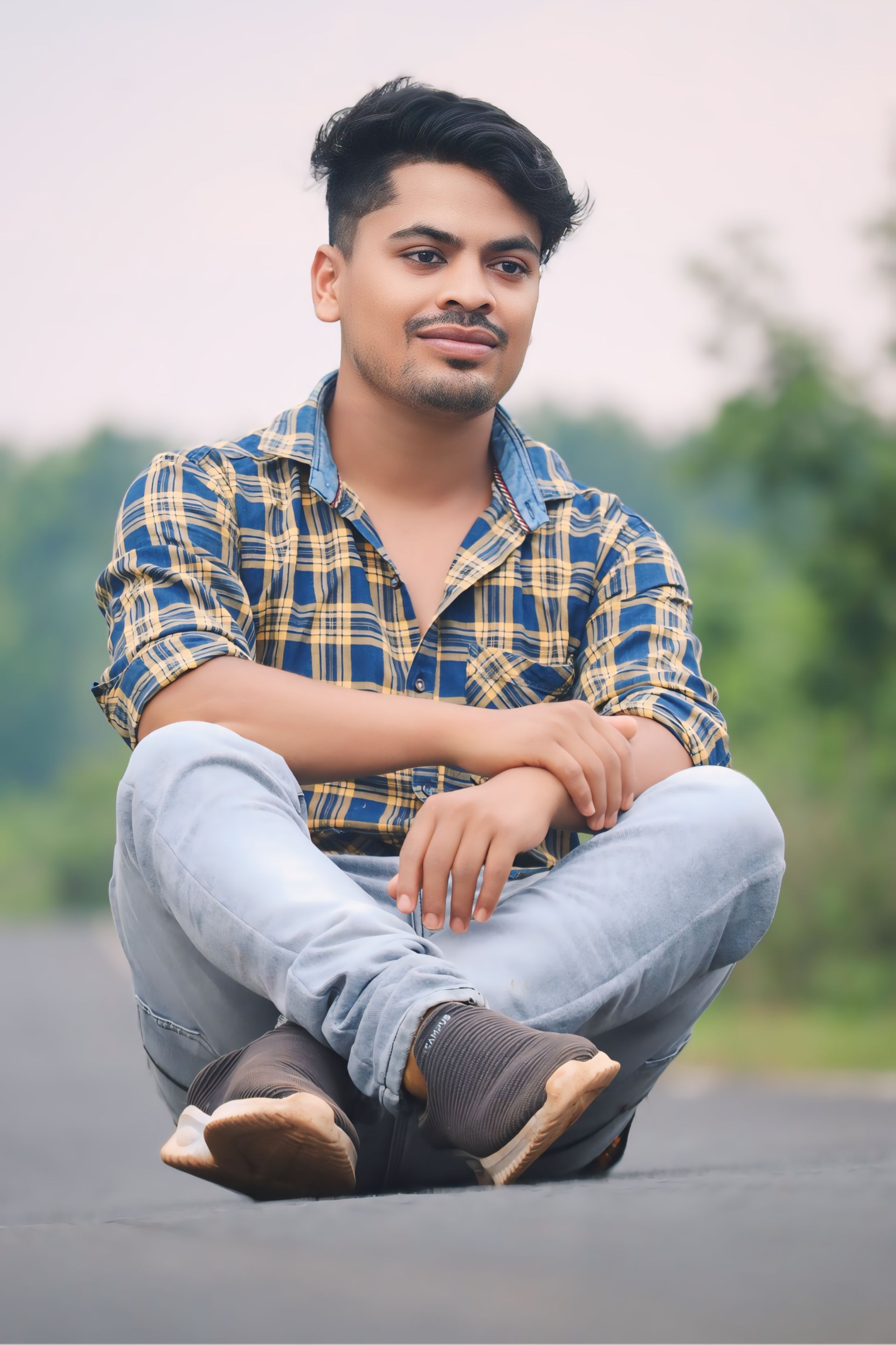 Casually dressed young man sitting cross-legged on a rural road in Kotapad, Odisha.
