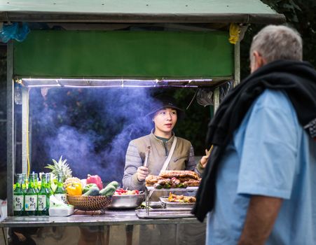 A street food vendor in Hoi An serves a customer at a bustling food cart.