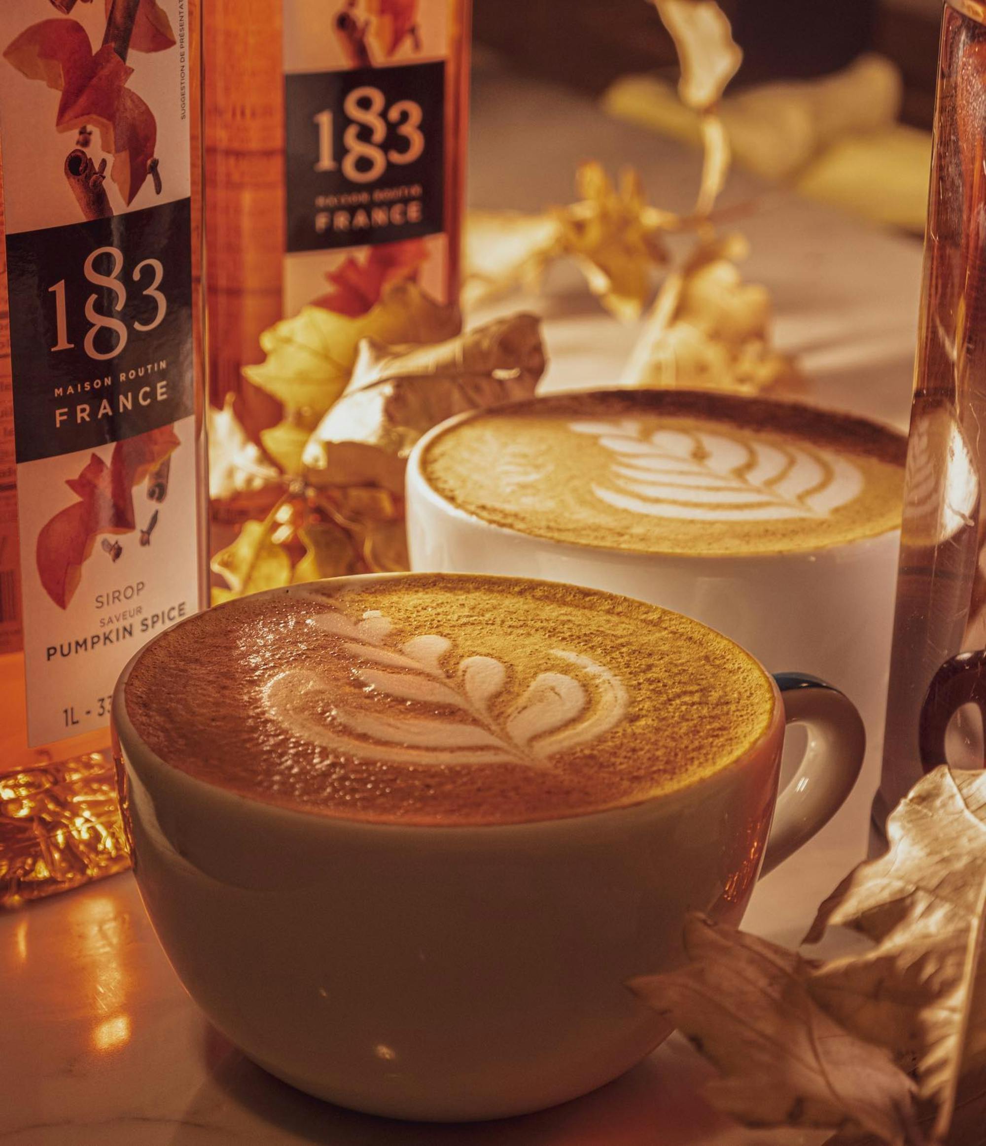 Warm latte art coffee with pumpkin spice syrup and autumn leaves on table.