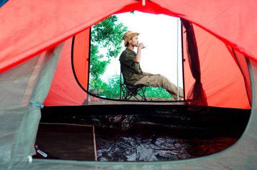 Free A man enjoys a peaceful moment sipping a drink while camping, surrounded by nature. Stock Photo