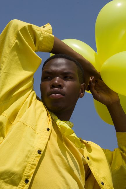 Dynamic shot of a man in yellow holding balloons against a clear sky.