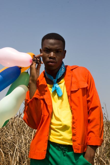 Colorful outdoor portrait of a man holding balloons, expressing a joyful vibe.