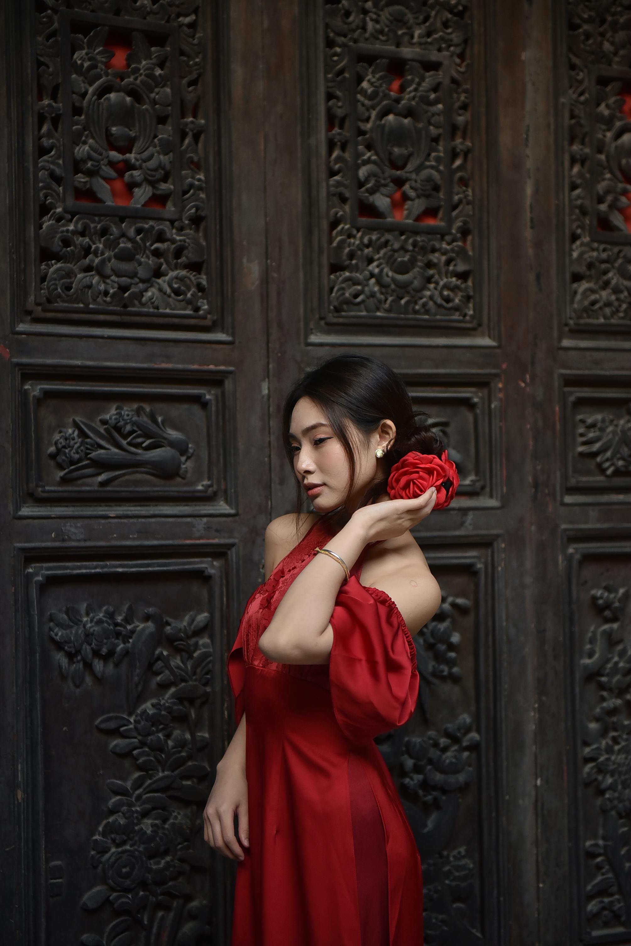 Elegant woman in a red dress stands gracefully with intricate carved wooden door backdrop.