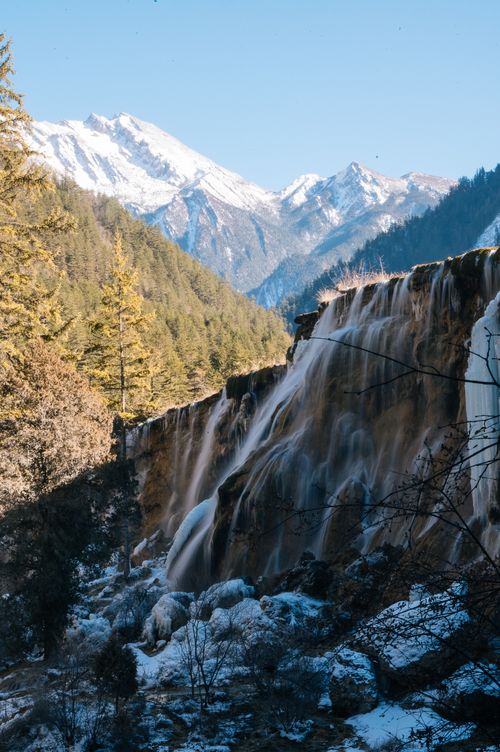 Free Stunning waterfall cascading down a mountain slope in a winter setting with snow-capped peaks. Stock Photo