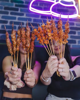 Two friends enjoying assorted grilled meat skewers indoors under neon lights.