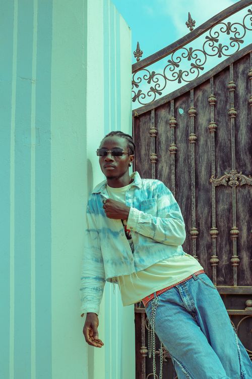 Free Stylish individual wearing sunglasses and jeans in Obuasi, Ghana with a decorative iron gate background. Stock Photo