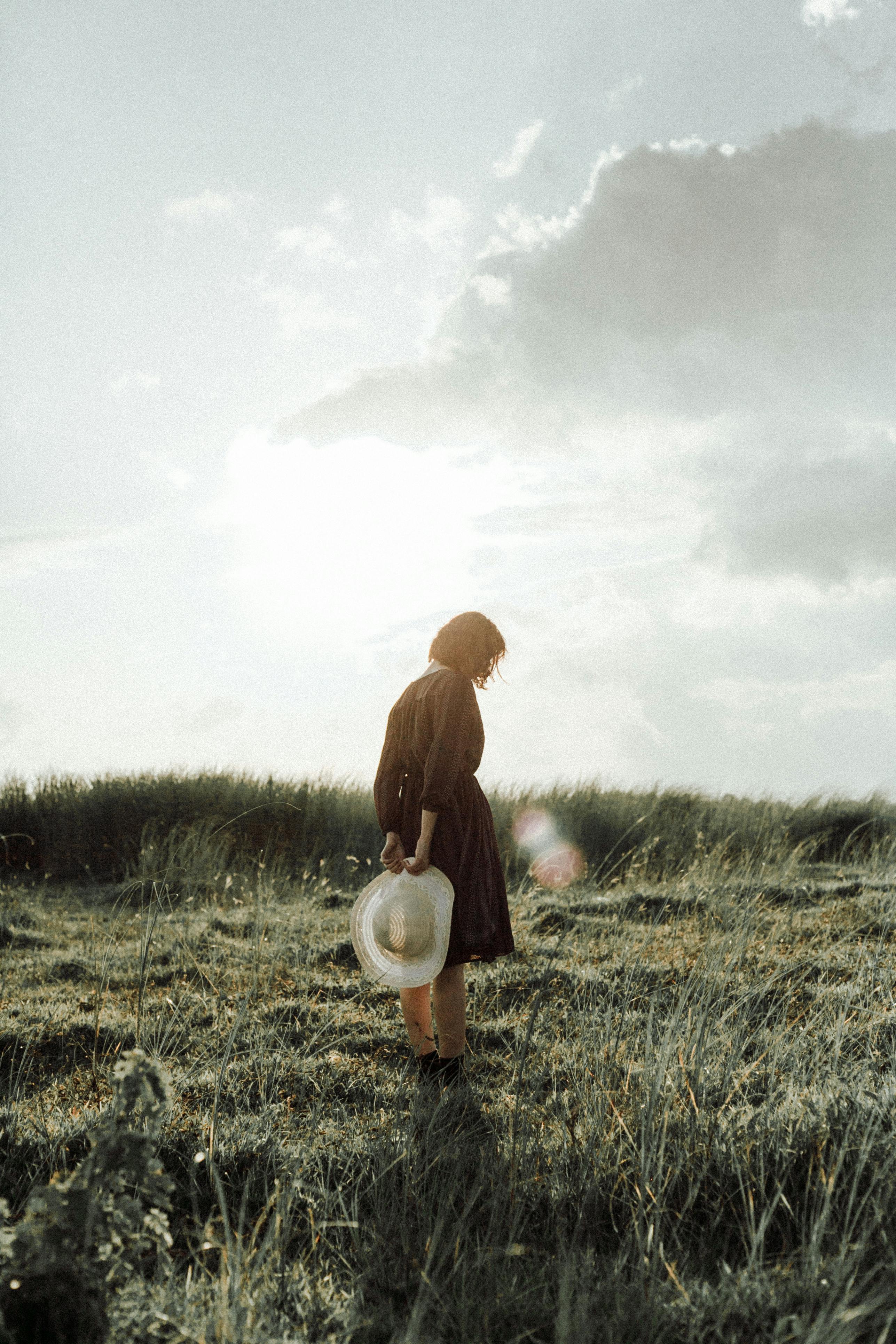 日落时分，草地上，一个女人戴着帽子，静静站立