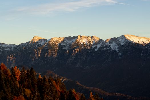 Stunning view of a sunlit mountain range with autumn foliage in the foreground.