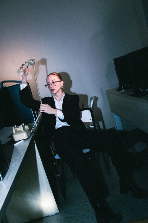 Free Woman in suit using a vintage phone in a dimly lit office. Stock Photo