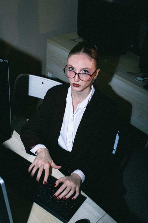 Free Businesswoman in office setting typing on computer, wearing glasses and formal attire. Stock Photo
