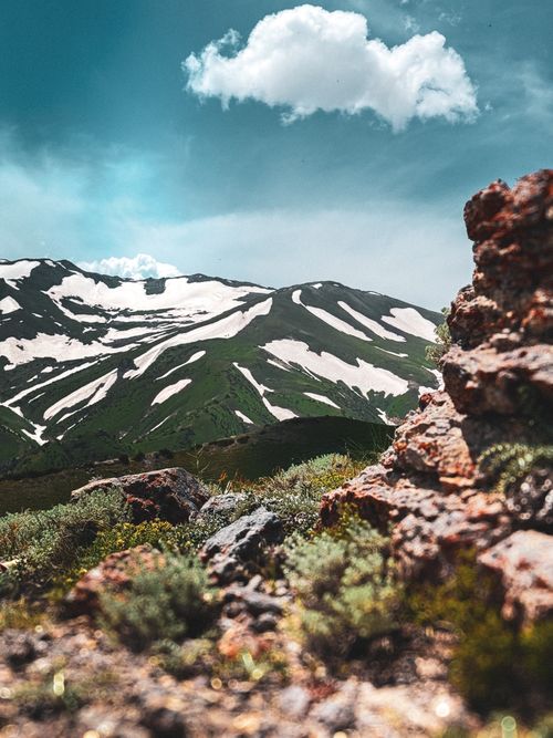 Free Breathtaking view of snow-capped mountains with vibrant green slopes and rugged rocks in the foreground. Stock Photo
