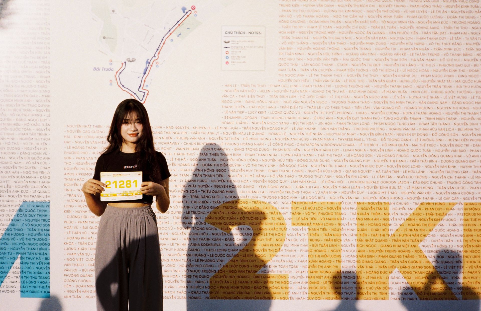 Girl holds race bib against backdrop of marathon course map in sunlight.