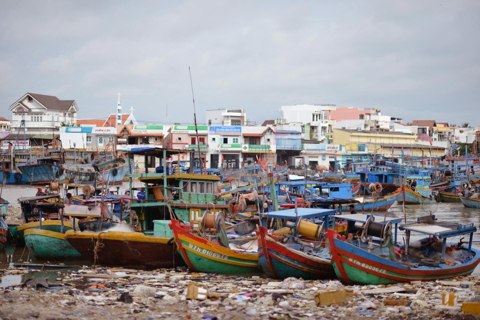 Vibrant fishing boats docked in a busy coastal village harbor with colorful buildings and market scene.