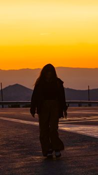 Silhouette of a person walking during a vibrant sunset with distant mountains and warm colors.