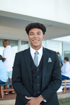Young man smiling in a suit at an outdoor social gathering.