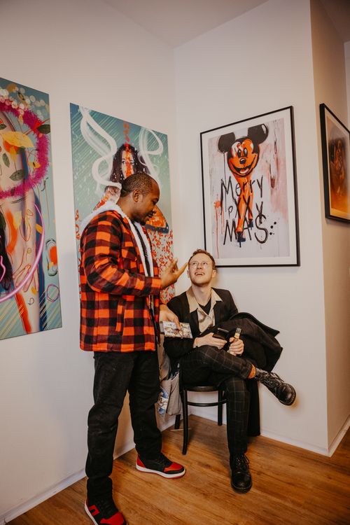 Free Lively art gallery event in Berlin featuring colorful graffiti-style artworks and a diverse crowd. Stock Photo