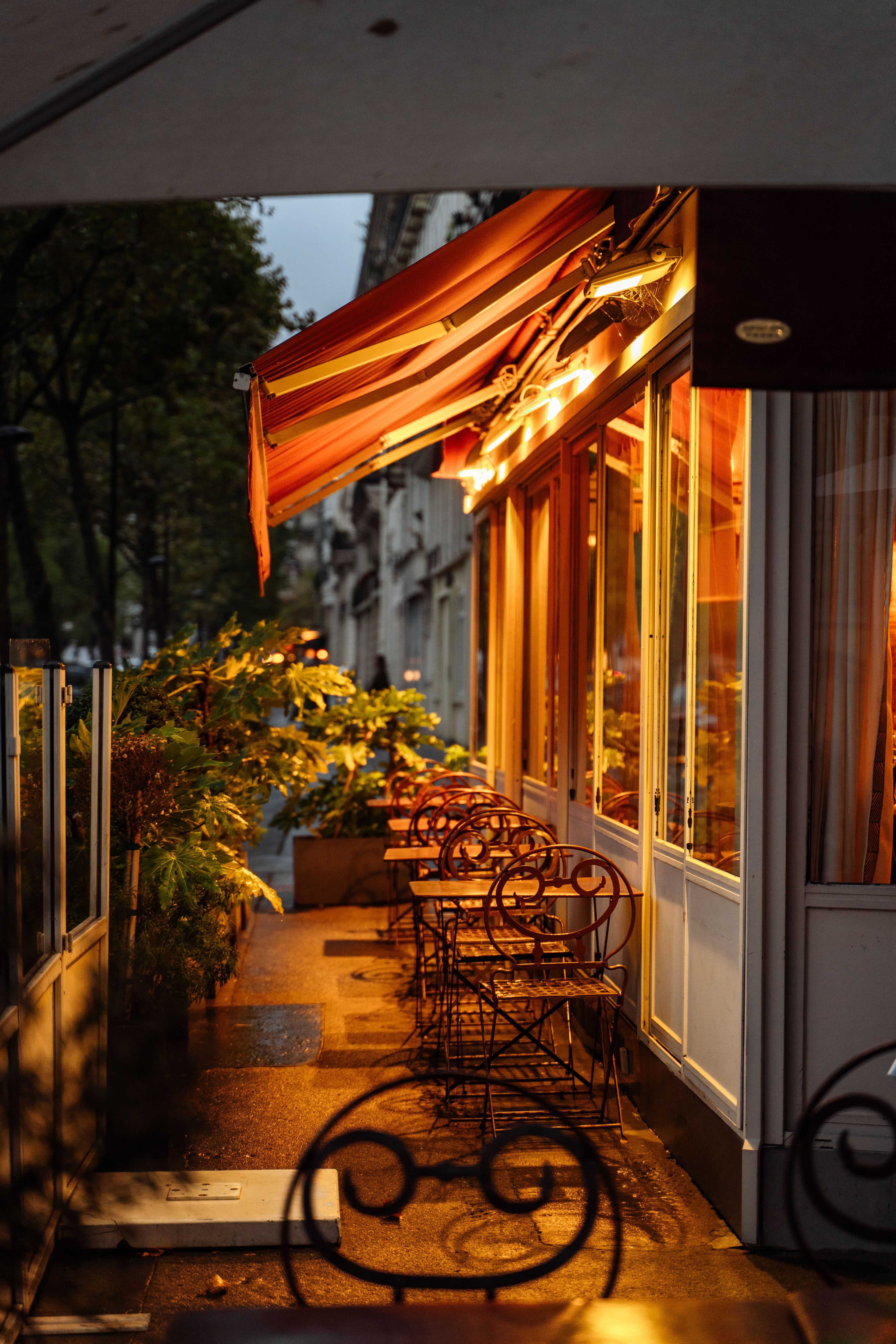 Terrasse de restaurant au soleil couchant, store orange et chaises de bistrot vides