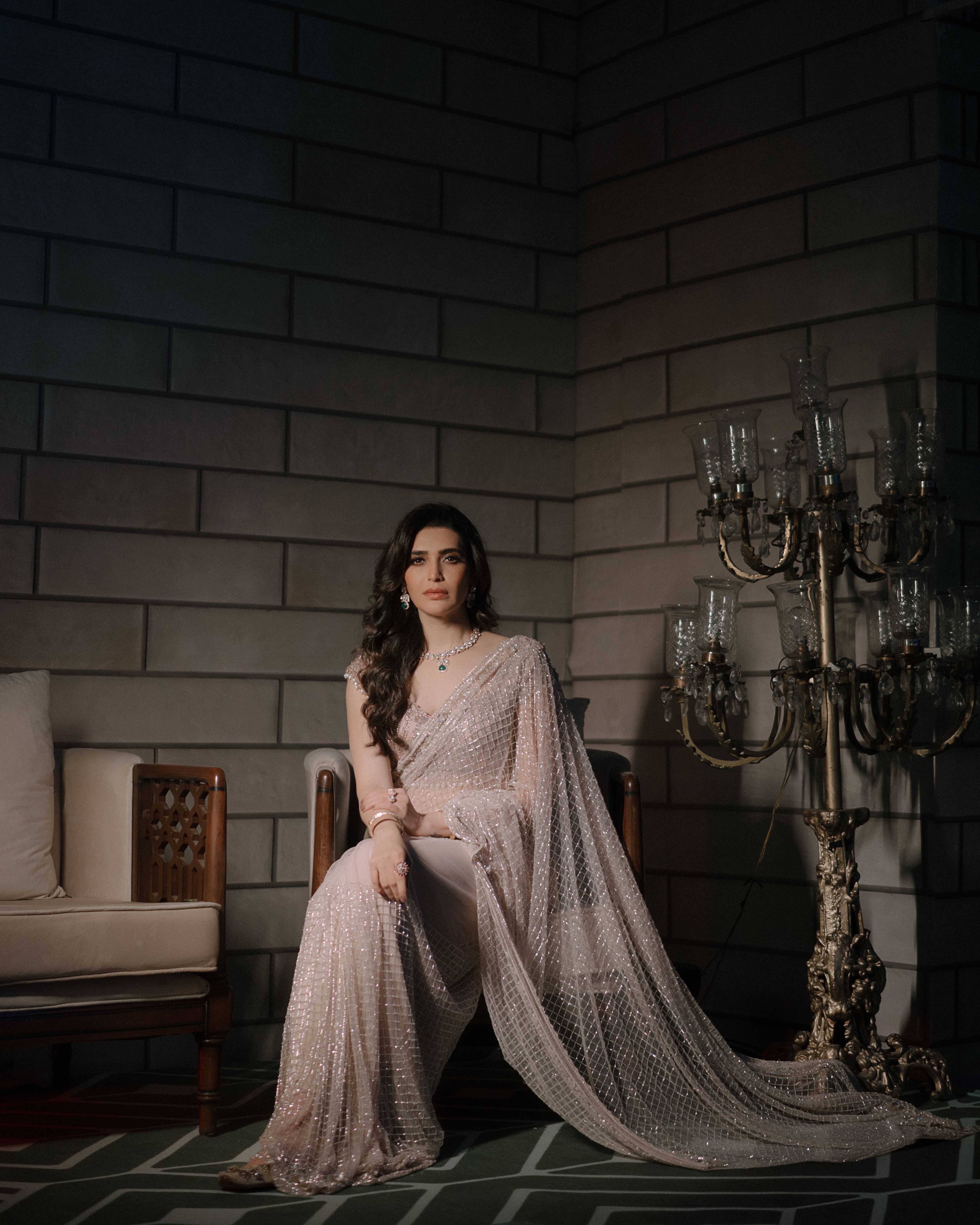 A woman in an elegant saree sitting indoors, exuding grace and poise.