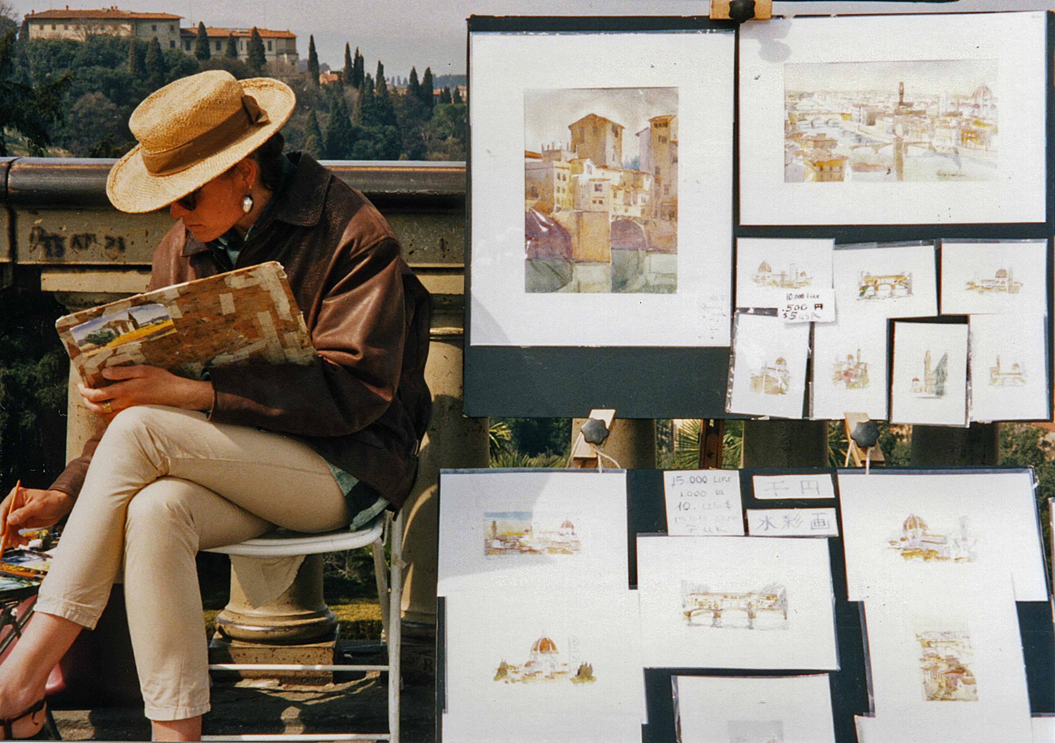 A street artist capturing scenic Florence with watercolors. Artworks displayed on easel outdoors.