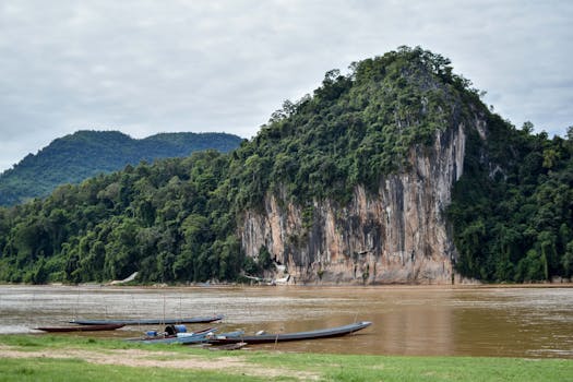 Longboats on the Nam Ou River with lush forested cliffs in Luang Prabang, Laos.