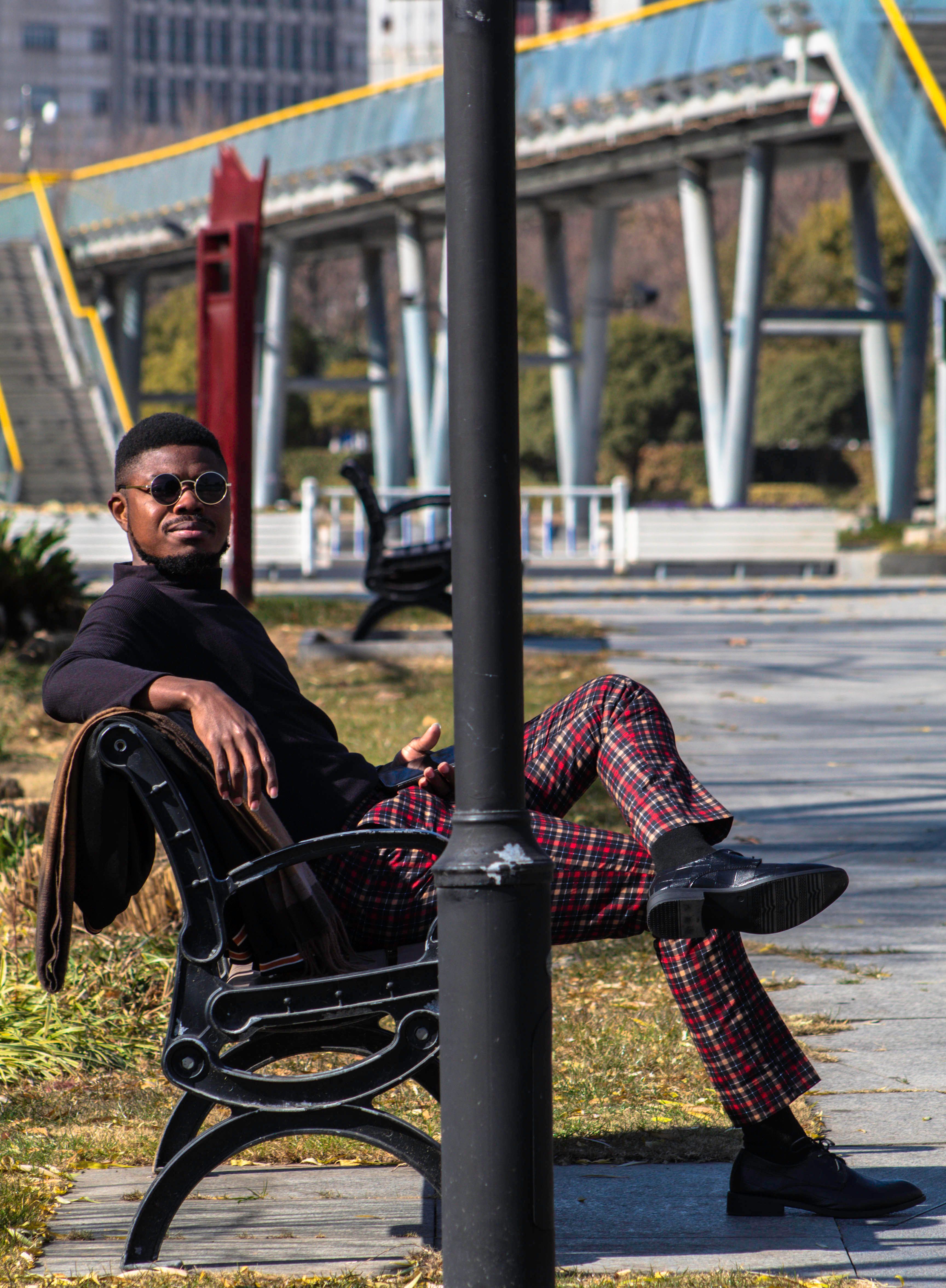 Stylish man in sunglasses sitting on a park bench in a modern city setting.