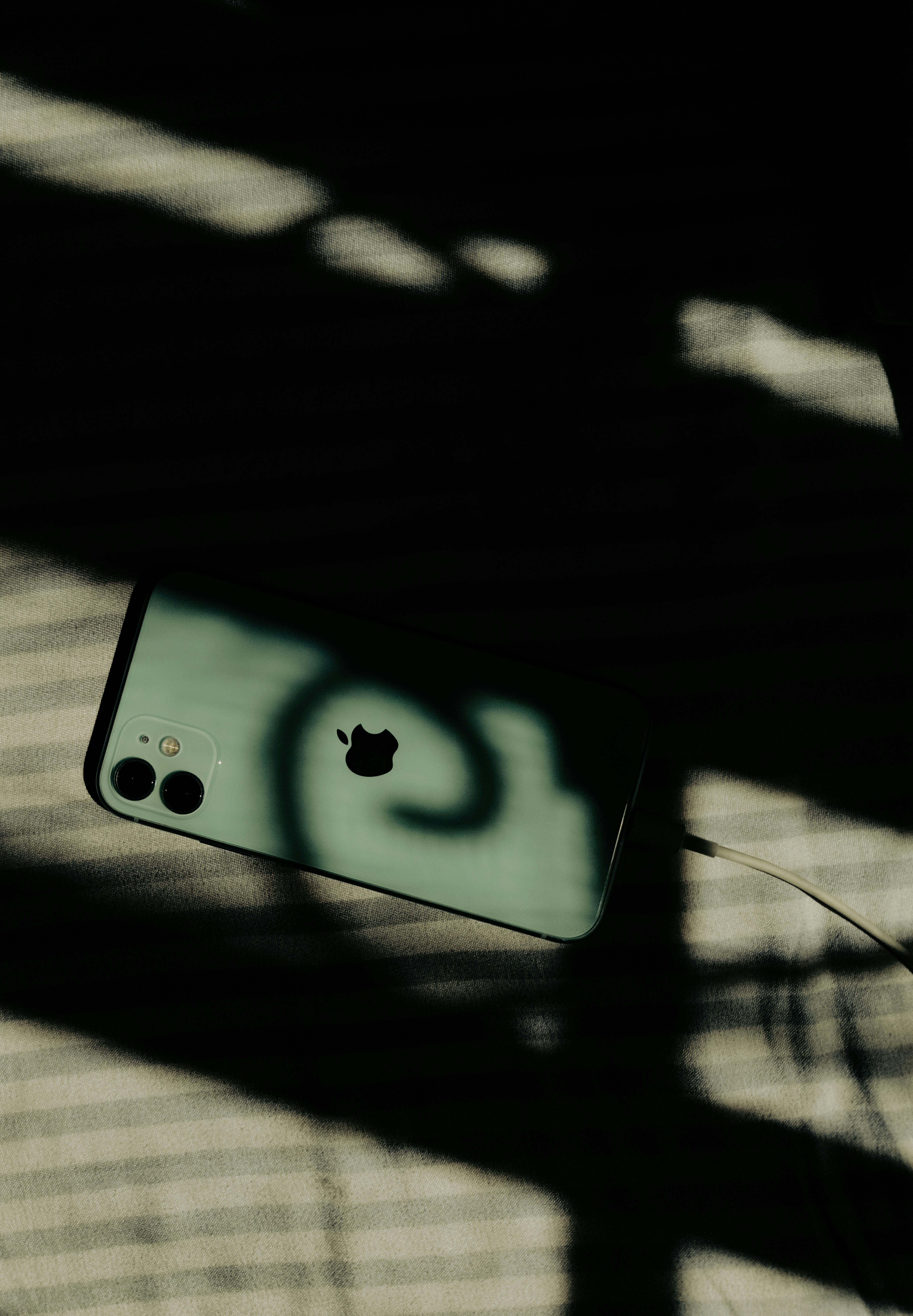 grátis Um smartphone com o logotipo proeminente da Apple projetando sombras dramáticas em uma superfície listrada. Foto profissional