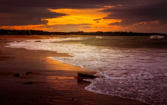 A breathtaking sunset casts vibrant hues over a serene beach scene.