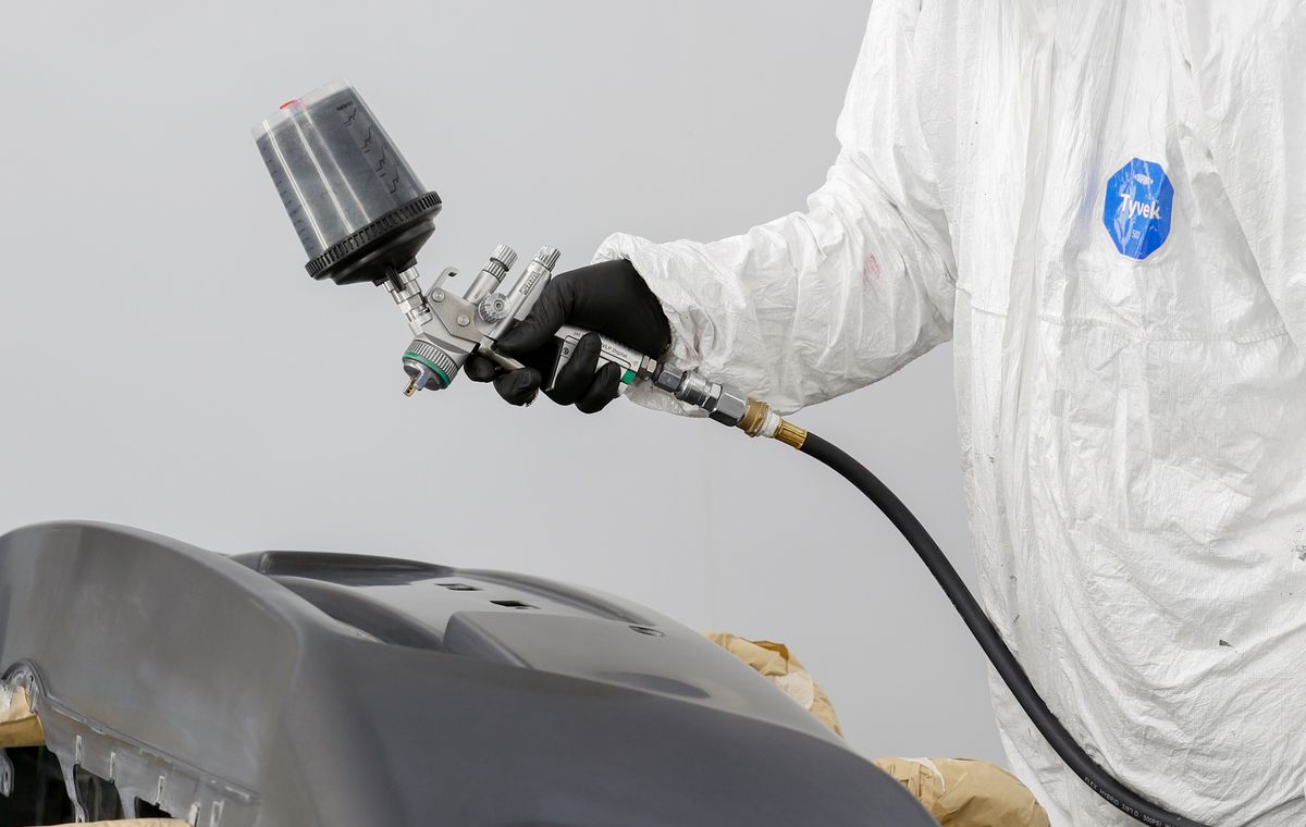Technician spray painting a vehicle panel inside a body repair workshop