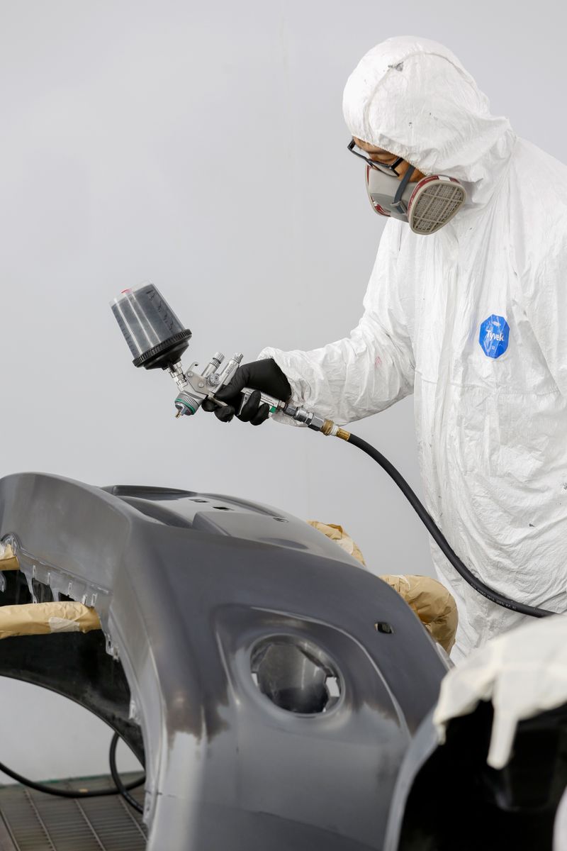 Technician spray painting a car bumper in a body shop