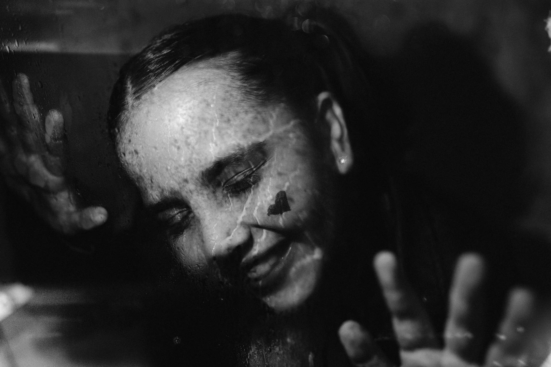 Black and white photo of a child smiling and pressing against a rainy window, conveying joy.