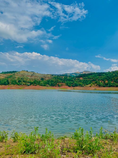 Free A scenic view of a tranquil lake with distant mountains and clear blue sky. Stock Photo
