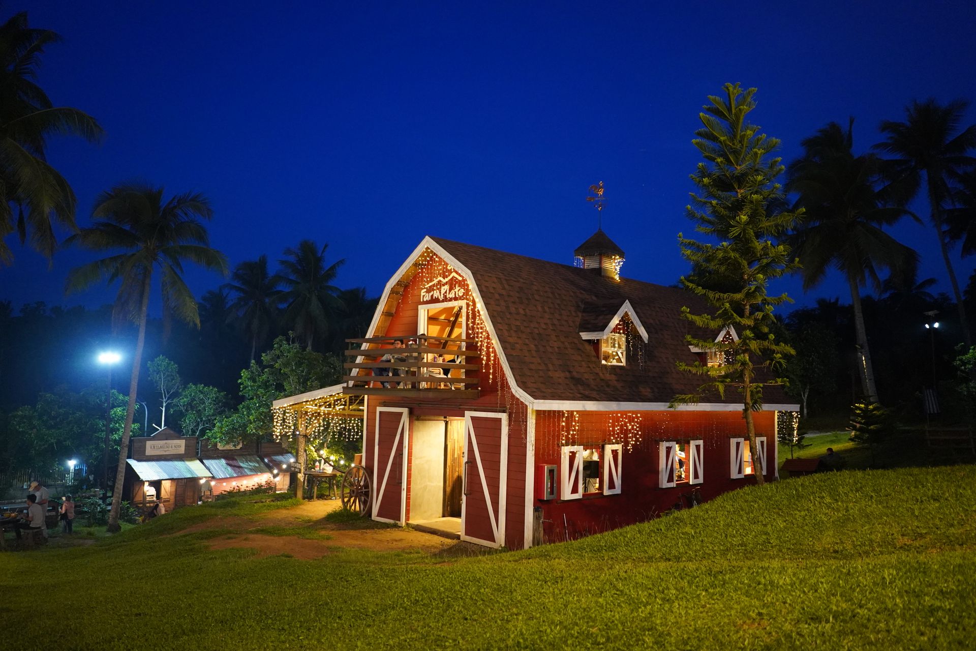 A charming red barn with lights surrounded by lush greenery under a clear night sky.