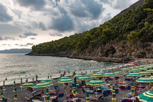 Colorful umbrellas dot a picturesque beach in Maratea, Italy, under a dramatic sky.