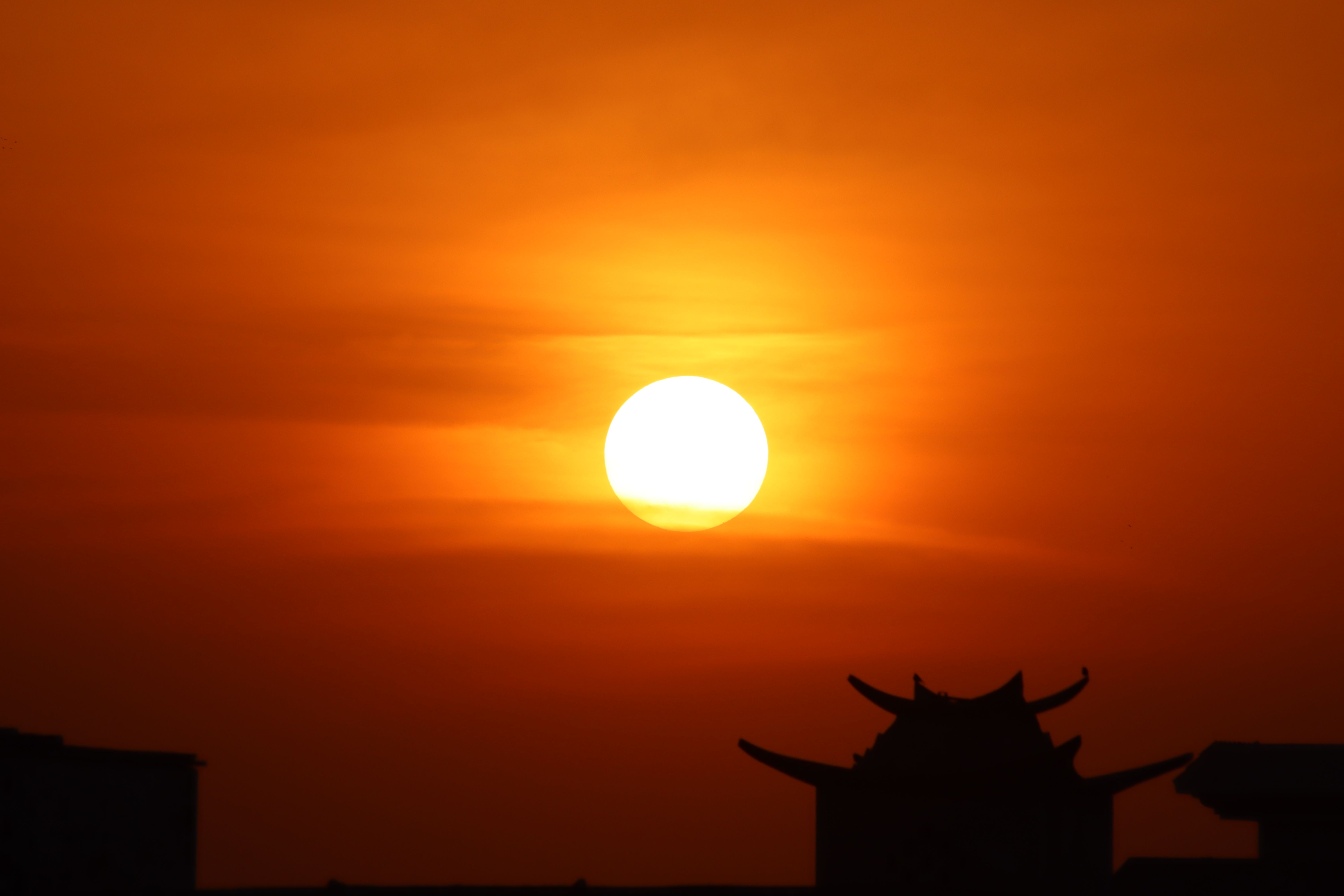 Beautiful sunset with dramatic orange hues and silhouetted rooftop, creating a serene atmosphere.